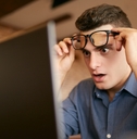 A man raises his glasses in shock at a computer screen