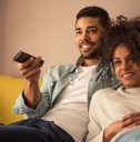 african american couple sitting on couch at home using remote while watching tv