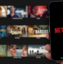 netflix logo on smartphone in man hand with movies in background