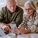 senior couple sitting at table using laptop while calculating expenses together