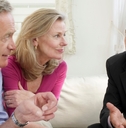 senior couple sitting on sofa with male financial advisor discussing documents