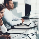 beautiful woman sitting at call center wearing headset talking to client with male colleague in background