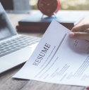 man sitting on table holding pen while reviewing resume at work