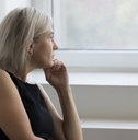 An older woman looks out the window in her home
