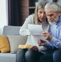 frustrated senior couple sitting on couch at home reviewing bills and taxes