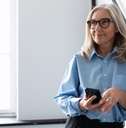 senior business woman standing on stairs at workplace while holding smartphone in hand