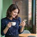 Woman smiling and holding a cup of coffee while looking at phone