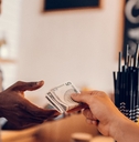 Smiling african american barista taking cash payment from customer on bar counter in cafe.