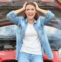 worried young girl holding her head in hands is standing infront of her red car that got out of order.