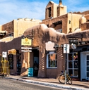 old town streets with adobe style architecture and sign boards besides cars on sidewalks in united states new mexico city during day time