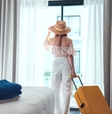 beautiful woman wearing sun hat checking into hotel room with luggage