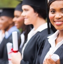 african american female student wearing graduation gown and hat with other students in background at graduation ceremony in college