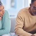 An elderly couple is sitting in the lounge of their house with documents, planning their tax and home budget with the help of a laptop and calculator.
