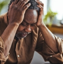 senior african american man sitting at table holding head in stress while looking at notebook