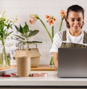 Young flower shop owner using laptop on counter while standing.
