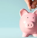 A hand puts a coin into a pink ceramic piggy bank.