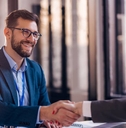 A businessman is shaking hands with a woman across a desk.