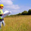 An architect in construction gear surving a new building plot.