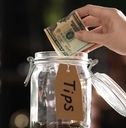 woman putting banknotes into glass jar