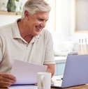 An older man sits in front of a laptop
