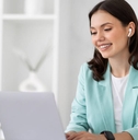 A woman typing on her computer and wearing a set of earbuds. 