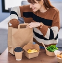 A woman sits at a coffee table and unpacks a food delivery order. She looks happy.