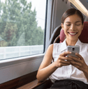 A woman smiles while playing on her phone on a train.