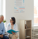 female doctor talking to senior couple while sitting in reception area of clinic