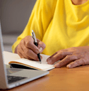 Senior woman writing note at desk with laptop
