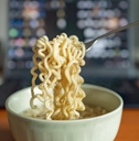 man eating ramen with laptop at work