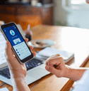 Man checking online bank account balance on smartphone while working on laptop at home