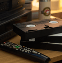 Close-up of several vintage VHS tapes stacked near remote control on wooden table with an old TV