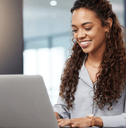 A woman smiles while typing on her laptop in an office setting.