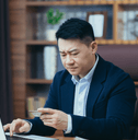 A man stares down at his credit card with his brows furrowed while sitting in his home office.