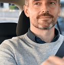 A man looks in the rearview while driving his car and gripping the steering wheel.