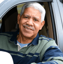 A senior rests his elbow out of his car&#x27;s window and smiles at the camera. 