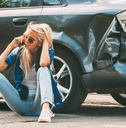 A woman places a phone call while she sits by the rear of her vehicle after a fender bender.