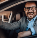 A man in a suit smiles in his car