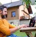 Side view of man with laptop working outdoors in garden, home office concept