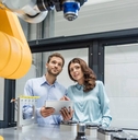 Colleagues in high tech company controlling industrial robots, using digital tablet