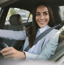 A woman in a suit smiles while she drivers her car.