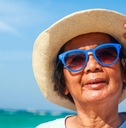 woman enjoys fun, visiting the sea, wearing a hat and wearing blue sunglasses