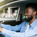 A young man in a blue button down grips the wheel and smiles.