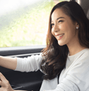 A woman with long brown hair smiles while driving her car.