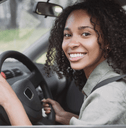 A young woman smiles while driving her car and wearing her seatbelt.