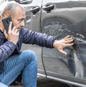 A man runs his hands over a dent in his car&#x27;s rear door panel.