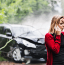 A woman clutches her head and calls someone on the phone after getting into a car accident.