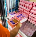 woman shopping in a grocery store grabbing a polystyrene foam carton of eggs from refrigerator