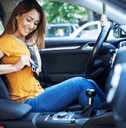 A woman in an orange shirt smiles as she puts on her seatbelt.