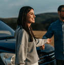 A couple stands in front of their vehicle while enjoying a mountain view.
